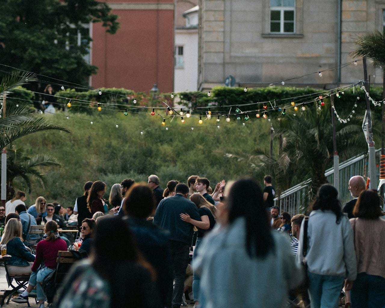 Enjoy a lively outdoor gathering with colorful lights and a diverse crowd at dusk in an urban setting.