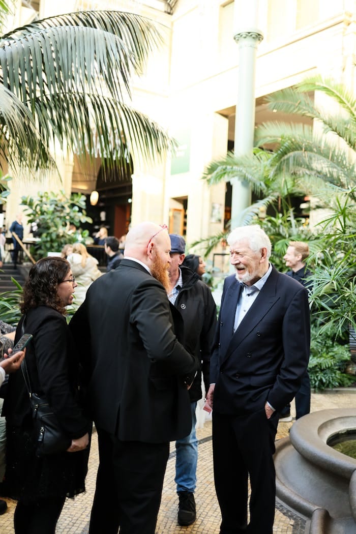 A group of adults engaged in conversation in a lush indoor atrium.
